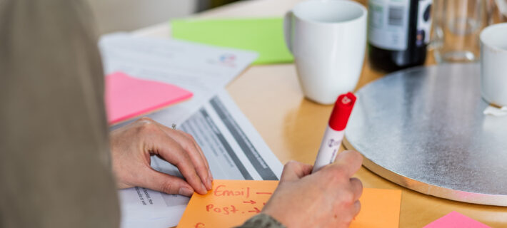 Photo is a close up image of a person writing with a thick marker pen on post it notes