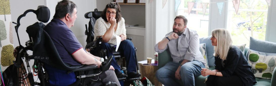 A group of four people engaged in a discussion at the Barnwood Trust Grants pre-launch event. Two participants are in wheelchairs, while the others two re seated on a sofa.