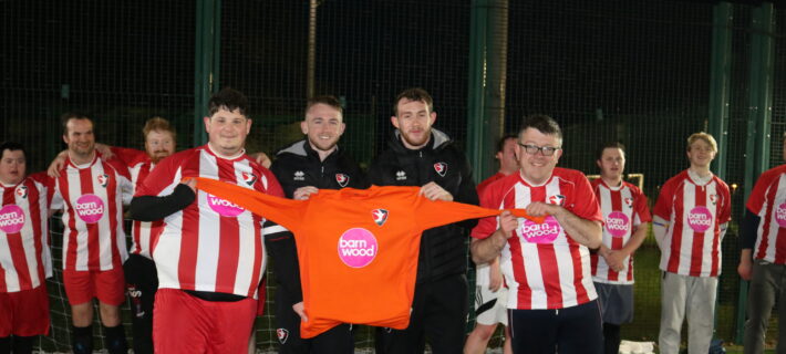 Cheltenham Town Community Trust's Adult Disability Football Team holding up their new football kit with the Barnwood logo on