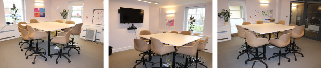 Photo gallery of meeting room with a square table in the middle and 8 seats around it with castors on and a screen on the wall in front of it.