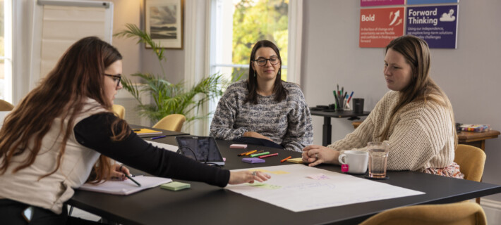 Three women in the research team discussing information on a large piece of paper